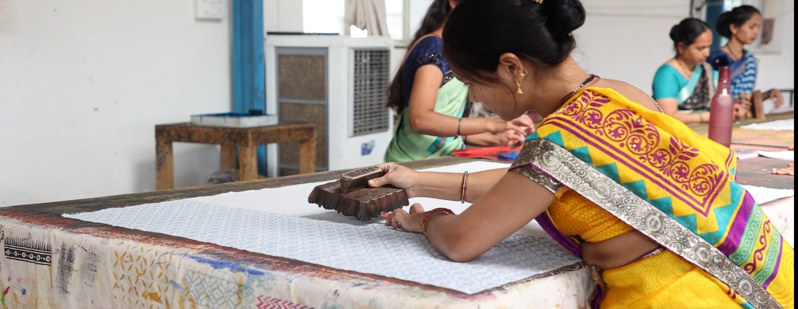 An artisan pressing a hand-carved wooden block onto cotton fabric during printing